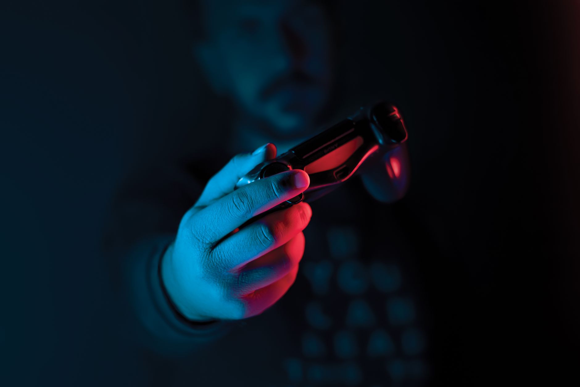 Close-up of a man's hand holding a joystick against a dark background with red and blue lighting. — How Digital Wallets Encou